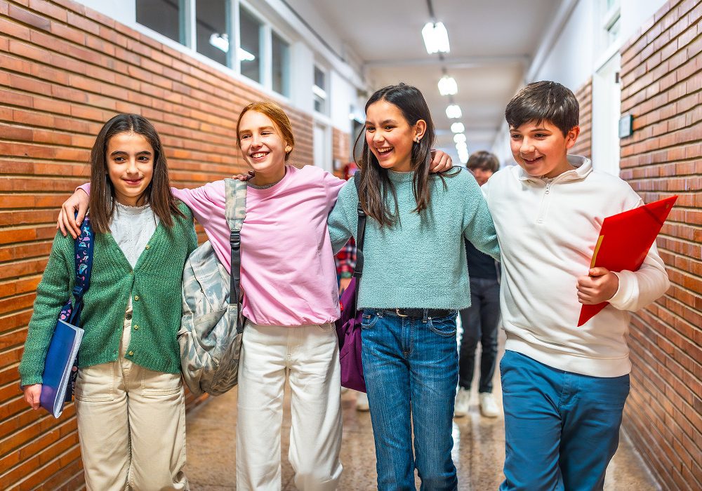 Four smiling students walking down school hallway